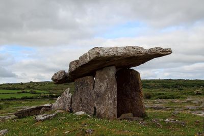 Stone structure on field against cloudy sky