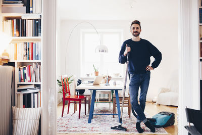 Portrait of happy man standing with vacuum cleaner in dining room at home