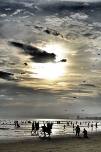 People at beach against sky during sunset