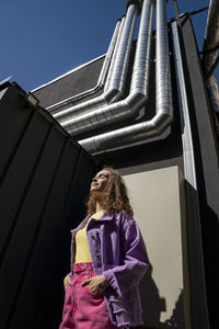 Woman with hands in pockets standing near building on sunny day