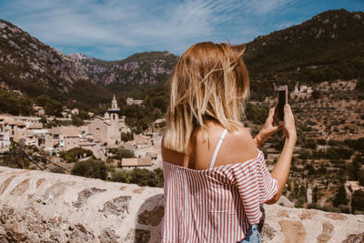 Rear view of woman using mobile phone against mountains