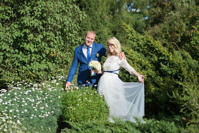 Portrait of smiling bride and groom standing amidst plants at park