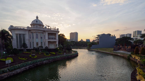 River amidst buildings against sky at sunset