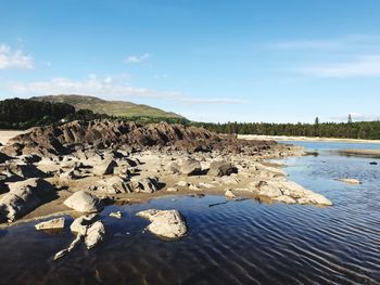 Rocks on shore by lake against sky