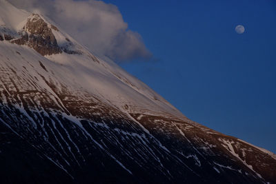 Low angle view of snowcapped mountain against blue sky