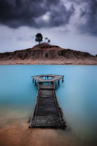 Gazebo in sea against cloudy sky