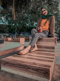 Full length of woman sitting on wood against trees