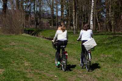 Rear view of friends riding bicycles on grassy field