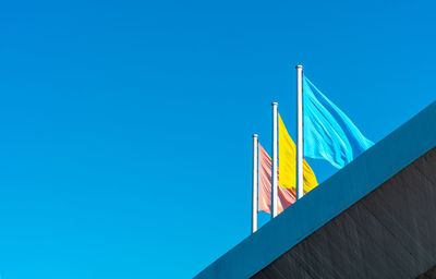 Low angle view of flags against clear blue sky