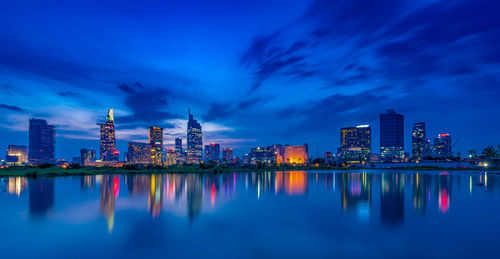 Illuminated buildings by lake against sky at dusk