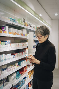 Senior female customer examining medicine by rack at pharmacy store