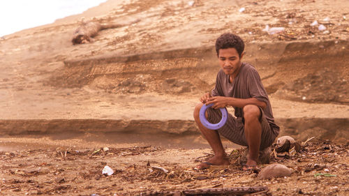 Full length of thoughtful homeless man holding plastic spool while sitting on land