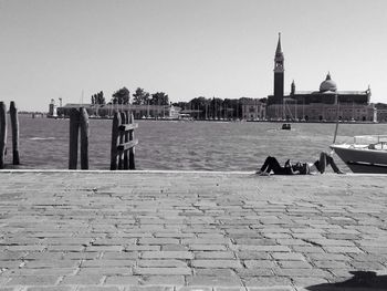 People on riverbank against clear sky in city