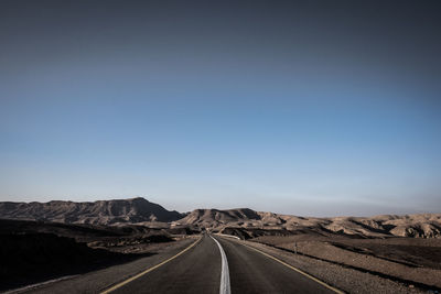 Road leading towards mountain against clear sky