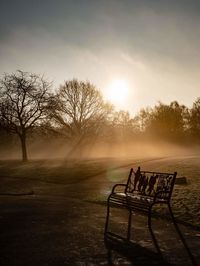 Empty bench in park against sky during sunset