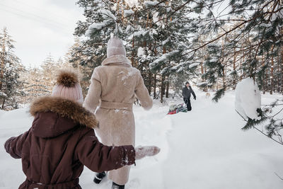 Dads roll their daughter on a sleigh, mom runs with her daughter through the snowy forest