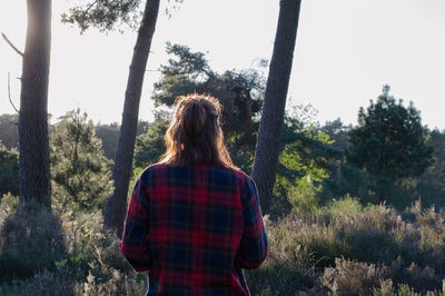 Rear view of woman standing by trees on grassy field