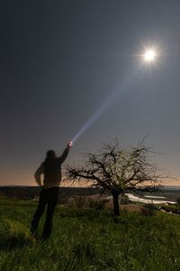 Rear view of man standing on field against bright sun