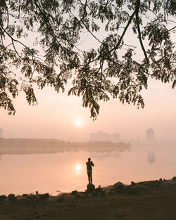 Silhouette man standing at lakeshore during sunset