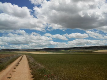 Road passing through field against cloudy sky