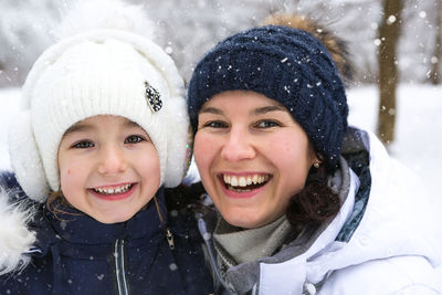 Mom and daughter in warm clothes in the snowy forest hugging and looking into the frame. winter 