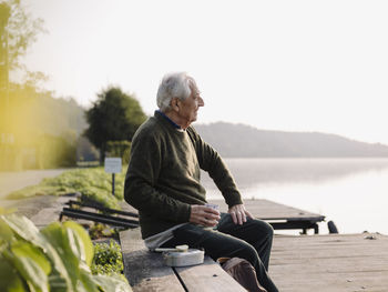 Full length of man sitting on mobile phone against sky