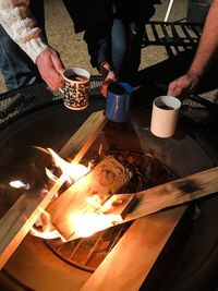 High angle view of friends holding coffee cup by bonfire at night