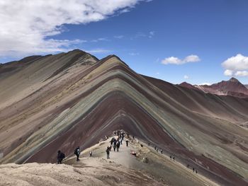 People walking on mountain against cloudy sky