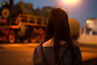 Rear view of woman standing on street against locomotive at dusk