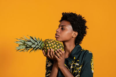 Young african american woman with short hair dressed in a summer shirt posing with pineapple