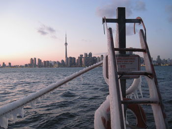 Frozen ladder by sea and cn tower against sky during sunset
