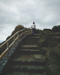 Rear view of woman walking on steps against sky