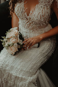 Midsection of bride holding bouquet while sitting on chair