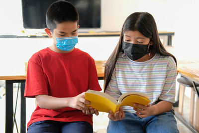 Asian boy girl student wearing face mask studying reading book in library. learning education 