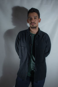 Portrait of young man standing against black background