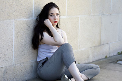 Portrait of young woman sitting against wall