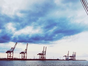 Cranes at commercial dock against sky