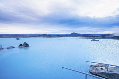 Scenic view of blue lagoon in geothermal spa against cloudy sky in valley