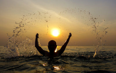 Silhouette man in sea against sky during sunset