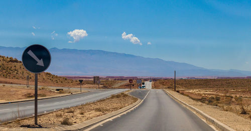 Country road leading towards mountains against sky