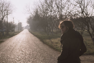 Woman walking on road amidst bare trees