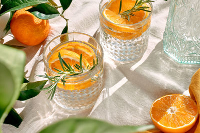 Summer refresh orange cocktail with ice, herb and ripe bio citrus fruits on linen tablecloth. 