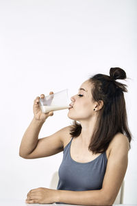 Portrait of young woman drinking glass against white background