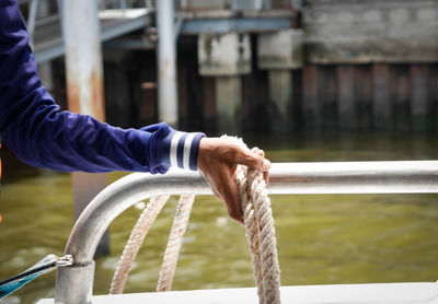 Cropped hand of man by rope against sea