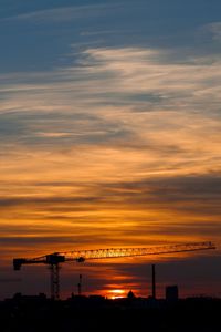 Silhouette cranes against sky during sunset