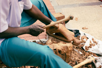 An african man carving a wooden figure in the streets of the city.