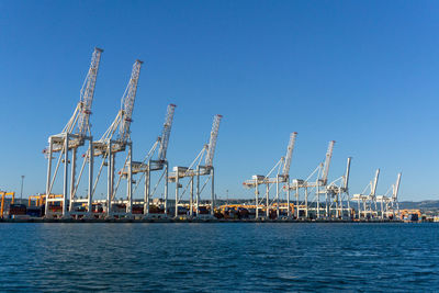 Cranes at commercial dock against clear blue sky