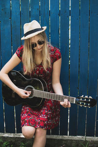 Teenager girl playing guitar while standing against wooden wall