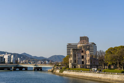 View of buildings by river against clear blue sky