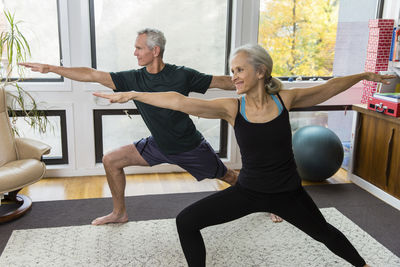 Couple with arms outstretched and legs apart exercising at home